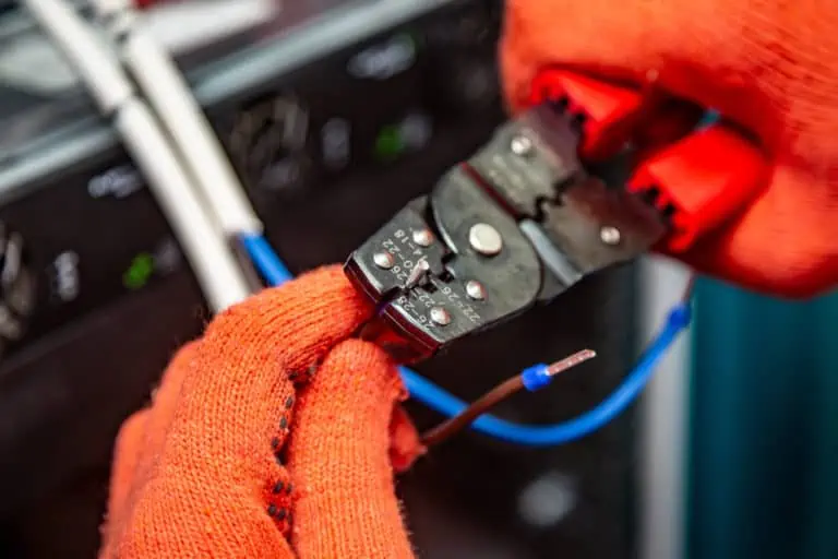 Hands in orange insulating gloves work with crimping pliers and cables. Horizontal orientation.